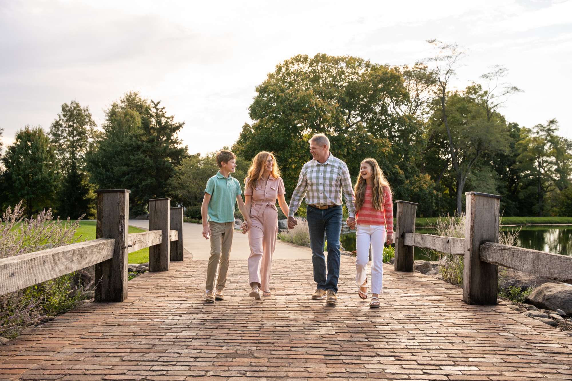 A family of four holding hands and laughing while walking across a brick bridge.