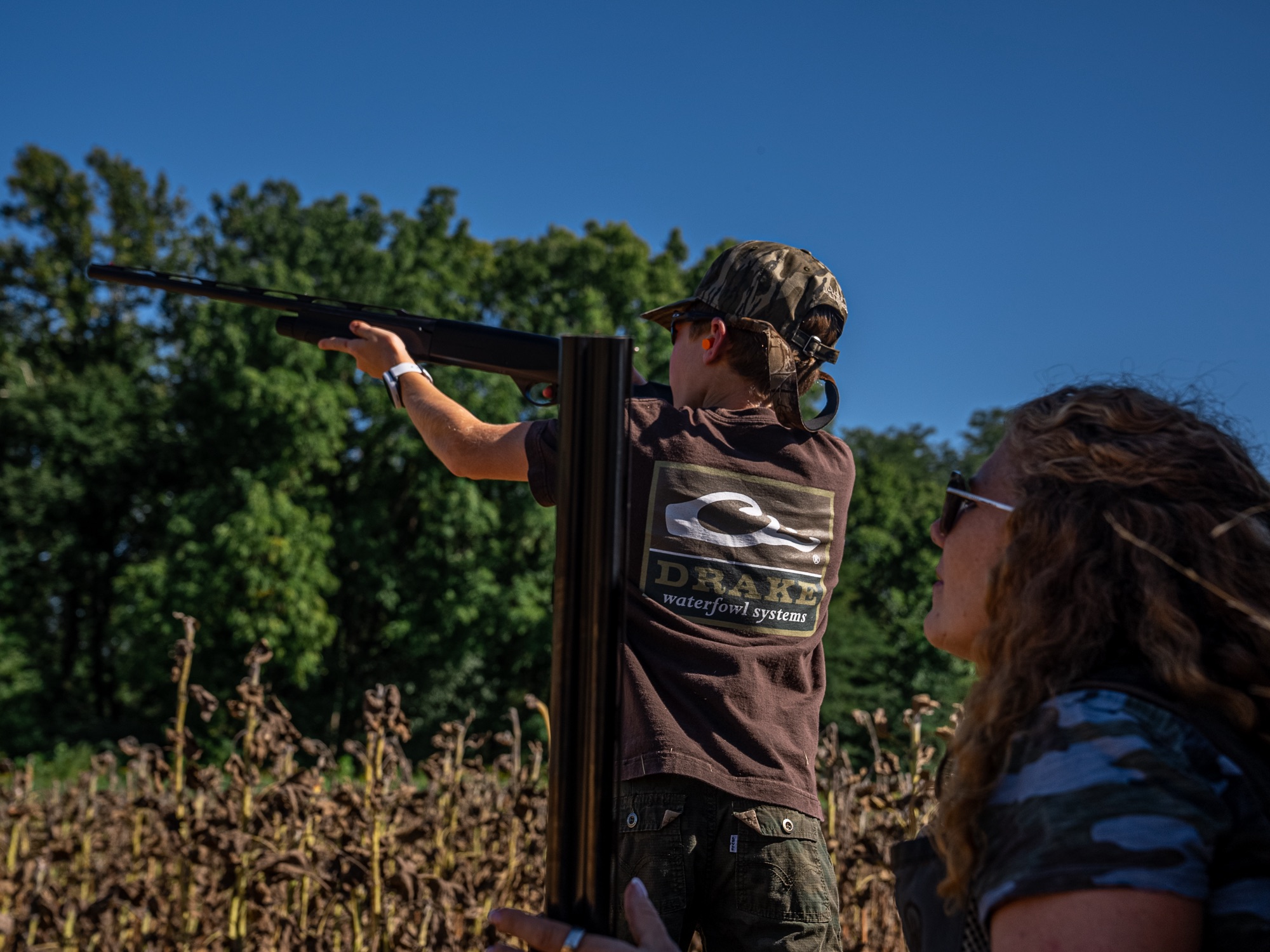 A family member taking aim during the Labor Day dove hunt, standing in a dried sunflower field, with Sara watching.