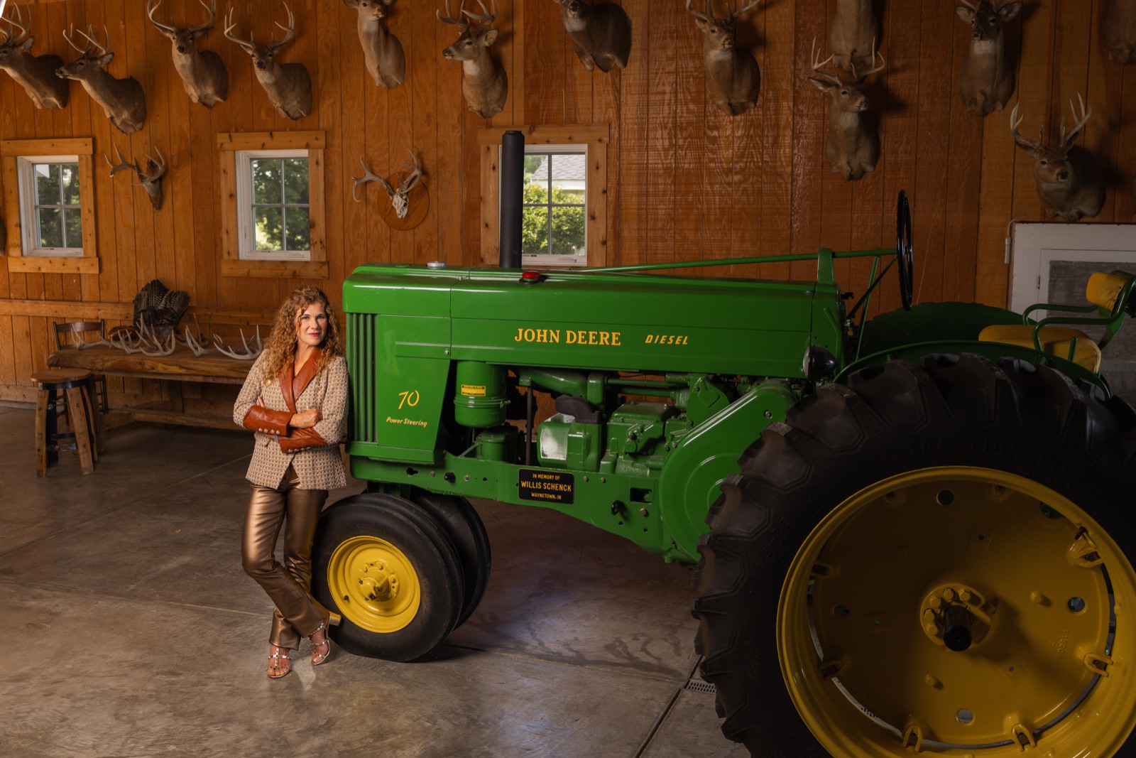 Sara standing beside a vintage John Deere tractor in a farm building.