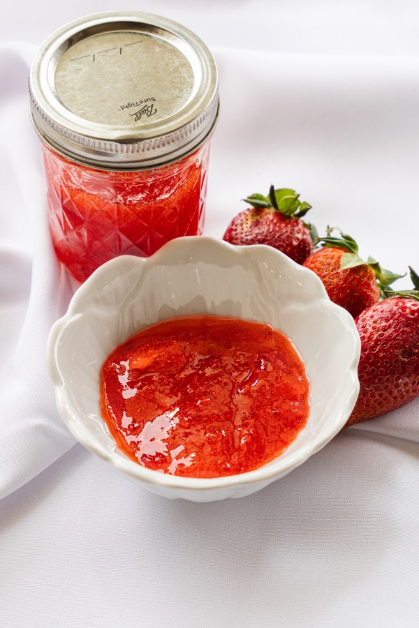 A jar of strawberry jam beside a bowl of fresh strawberries.